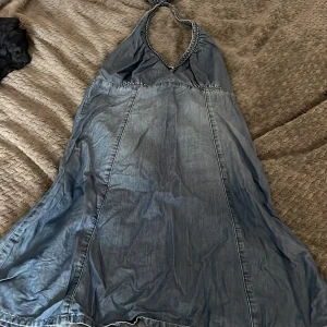 Blå halterneck klänning i jeans - Snygg blå halterneck klänning i jeansmaterial med knyt i nacken och v-ringad hals. Klänningen har en lätt utställd passform och sömdetaljer som ger en cool look. Perfekt för dig som gillar avslappnad men trendig stil. Sitter jätte snyggt på men tyvärr inte min stil❤️