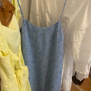 Blå långklänning perfekt till sommaren! - Supersöt långklänning i ljusblått med tunna axelband och små blå blommor över hela tyget. Klänningen har en rak, flowy passform och är perfekt för varma dagar. Materialet känns lätt och svalt, vilket gör den extra skön att bära. Knappt använd💛