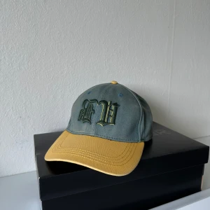 Baldi keps i grön och gul bomull - Snygg keps från Baldi i grön bomull med gul skärm och broderad logga framtill. Skärmen har även texten 'BALDI' broderad undertill. Klassisk sexpanel-design med justerbar passform och coola kontrastfärger. Perfekt accessoar för en streetwear-look.