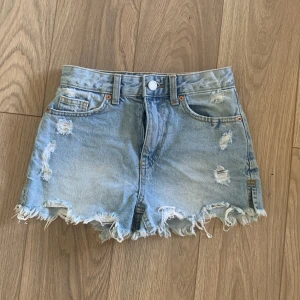 Ljusblåa jeansshorts från FB Sister - Snygga ljusblåa jeansshorts från FB Sister i storlek XXS. De har hög midja, slitna detaljer och fransig kant nedtill. Klassisk femficksmodell med knapp och dragkedja framtill. Perfekta för varma sommardagar!