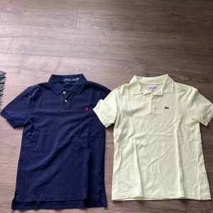 2 pikétröjor Polo Ralph Lauren & Lacoste - Två klassiska pikétröjor: en marinblå från Polo Ralph Lauren med röd logga och slim fit, samt en ljusgul från Lacoste med broderad krokodil. Båda har kort ärm, krage och knappar framtill. Perfekta för en clean och sportig look.