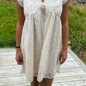 Vit kortklänning från Shein Frenchy - Supersöt vit kortklänning med v-ringning och volangärmar från Shein Frenchy. Klänningen har ett diskret strukturmönster och är lätt och luftig, perfekt för varma dagar. Den har en lös passform och är tillverkad i ett tunt, syntetiskt material.