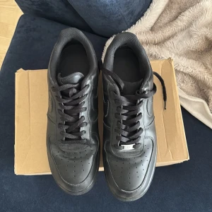 Nike Air Force 1 helsvarta sneakers - Säljer ett par klassiska Nike Air Force 1 i helsvart skinn med svart sula och svarta skosnören. Modellen har den ikoniska swoosh-loggan på sidan och perforerad tå för extra ventilation. Perfekta för dig som gillar en clean och tidlös look. Pris går att diskutera och ni bor i Stockholm adda melito_siri 