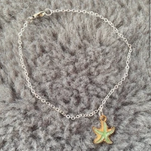 Armband med sjöstjärna i guld och grönt - Snyggt armband med tunn silverfärgad kedja och en hängande sjöstjärna i guld och ljusgrönt. Perfekt accessoar för dig som gillar havsinspirerade detaljer och vill ha något unikt på handleden.