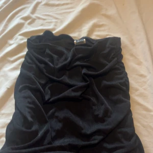 Svart kort klänning från SHEIN XS - Säljer en svart, tight och kort klänning från SHEIN i storlek XS. Klänningen har snygga rynkade detaljer längs sidorna och är gjord i ett stretchigt material som sitter figurnära. Perfekt för dig som gillar en enkel men ändå trendig look.