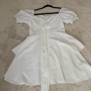 Vit kortklänning med puffärm från SHEIN - Superfin vit kortklänning från SHEIN med puffärmar och markerad midja. Klänningen har volangig kjol i två lager och ett brett band framtill. Söt och trendig modell med fyrkantig ringning och elastiska ärmslut. 