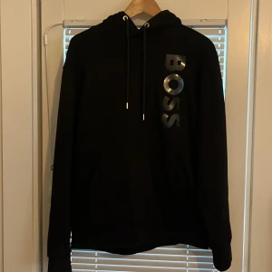  BOSS hoodie  - Svart hoodie från BOSS i storlek M passar också mig som är S men sitter ganska bra på både M, med stort glansigt BOSS-tryck vertikalt på bröstet. Klassisk Luva med snörning och långa ärmar. Perfekt för dig som gillar stilrena look som inte skriker för mycket, hoodien är köpt från boss för ett år sedan där jag köptden för 2800. Priset kan dessutom diskuteras är inte omöjlig o förvandla med.