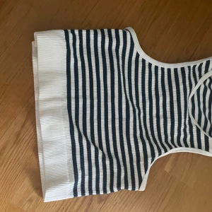 Randig ribbad linnetopp Pull&Bear - Säljer en ribbad linnetopp från Pull&Bear i marinblått och vitt. Toppen har smala axelband och ett klassiskt randigt mönster. Perfekt för varma dagar och enkel att matcha med jeans eller shorts.