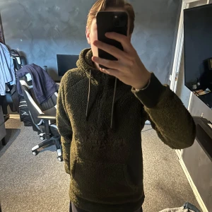 Olivgrön fleecehoodie Peak Performance - Säljer en olivgrön hoodie från Peak Performance i mjuk teddyfleece. Tröjan har broderad logga på bröstet, stor huva med snörning, magficka och half zip-dragkedja. Perfekt för kalla dagar och chill vibes. Inte använd så mycket strl s 