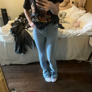 Ljusblå bootcut jeans - Säljer ett par ljusblå jeans med bootcut-modell och hög midja. Jeansen har klassisk femficksdesign och är tillverkade i stretchigt denimtyg som sitter snyggt och bekvämt. Perfekta för dig som gillar en retroinspirerad look med smal passform upptill och utsvängda ben.