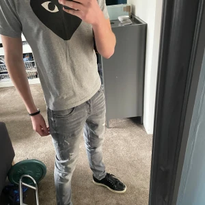 CDG T-shirt - Säljer en grå t-shirt med ett stort svart hjärta med ögon tryckt på bröstet. T-shirten har rund halsringning och korta ärmar. Materialet känns mjukt och skönt, perfekt för en chill look.Storlek L men passar som M. Priset är inte hugget i sten!