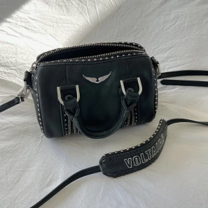 Sunny Nano Studs Bag  - INTRESSEKOLL på min svarta handväska från Zadig & Voltaire i äkta skinn med silverfärgade metalldetaljer, dubbla handtag och avtagbar axelrem med broderad logga. Väskan har dekorativa dragkedjor och nitar längs kanterna samt ikonisk vinglogga framtill. 🤎säljer den då den tyvärr inte kommer till användning.  