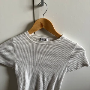 Vit ribbad topp från Stradivarius - Superfräsch vit ribbad topp från Stradivarius i storlek XS. T-shirten har korta ärmar, rund halsringning och är gjord i ett stretchigt, mjukt material som sitter snyggt på kroppen. Perfekt att styla med jeans eller kjol för en clean look.