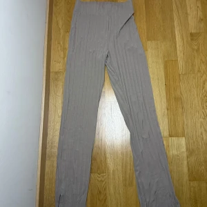 Ribbade beige mjukisbyxor från Gina Tricot - Superbekväma ribbade mjukisbyxor i ljus beiges från Gina Tricot. Byxorna har hög midja, raka ben med slits nertill och är gjorda i mjukt bomullsmaterial. Perfekta för chill dagar eller när du vill ha en avslappnad look.
