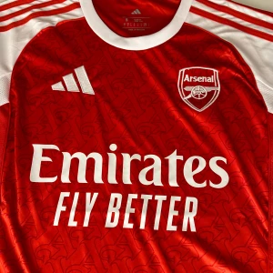 Arsenal hemmatröja 25/26 - Letar du efter en Arsenal-tröja med riktigt bra kvalitet? Då har du kommit rätt! Hos oss på BallerDrip hittar du Arsenal-tröjor i alla storlekar, perfekt för både barn och vuxna – oavsett om du är på läktaren, på planen eller bara vill representera ditt favoritlag med stil.  ✅ Alla storlekar i lager ✅ Bästa kvaliteten i hela Sverige ✅ Snabb leverans & grymma priser  Du hittar inte bättre kvalitet någon annanstans i Sverige – det vågar vi lova! Passa på innan storlekarna tar slut!