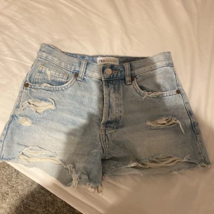 Ljusa jeansshorts med slitningar från Zara - Snygga ljusblå jeansshorts från Zara med råa kanter och slitna detaljer framtill. Klassisk femficksmodell med hög midja men jätte snygga att vika ner till lågmidjad. Perfekta för sommardagar när du vill ha en chill och trendig look.