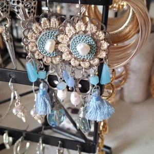 Blå boho örhängen med pärlor - Unika örhängen i boho-stil med silverfärgad metall, ljusblå detaljer, pärlor och små tofsar. De har blommig form och hängande dekorationer i olika blå nyanser, pärlemor och glasliknande material. Perfekta för dig som gillar statement-smycken.