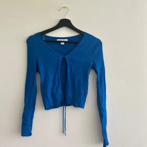 Blå ribbad bolerotopp från Amisu - Snygg blå bolerotopp från Amisu med ribbad struktur och lång ärm. Toppen har v-ringning och knytband framtill för en trendig look. Perfekt att styla med höga jeans eller kjol för en cool vibe.