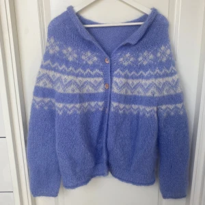 Ljuslila stickad kofta i alpacka ull  - Supermysig ljuslila stickad kofta med vita nordiska mönster och träknappar framtill. Koftan har lång ärm och är fluffig och mjuk, perfekt för kyliga sommarkvällar eller vinterdagar. 