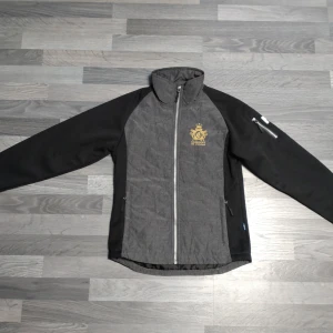 Cassilove of Sweden grå vindjacka / ridjacka - Quiltad vårjacka från Cassilove Of Sweden, knappt använd så mycket fint skick.  Detaljer:  - Ärmarna är gjort av softshell, tre lager, som andas.  - Sverige flagga på ärm och nacke.  - Snygg dragkedja med detalj.  - kardborrespänne på ärm för att justera storlek nertill på ärmen.   * Jackan är slimmad modell, så den kan uppfattas som liten i storlek.   Ordinarie pris, 1895:-  