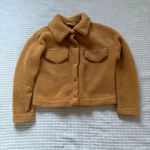 Gul teddyjacka från Gina Tricot XS - Supermjuk teddyjacka i Gul från Gina Tricot. Jackan har klassisk krage, två bröstfickor med lock och stängs framtill. Perfekt för lager-på-lager och ger en chill vibe till din outfit.