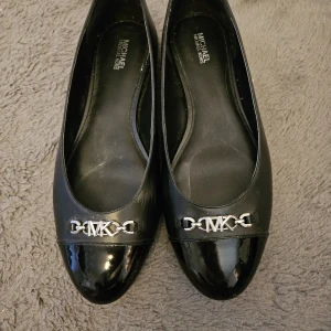 Michael Kors Ballerinaskor - Svart - Eleganta svarta ballerinaskor från Michael Kors. Perfekt för både vardag och fest. Klassisk design med en dekorativ MK-logga framtill. Inköpta våren 2025 på zalando för 1695 kr , Använda fåtal ggr men finns tecken på användning. Går säkert att putsa bort. Syns mer på bilderna än i verkligheten