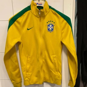 Brasilien track jacket - Gul Brasilien-jacka från Nike med gröna detaljer på axlar och ärmar. Storleken är S men den är liten i storleken så jag skulle säga mer XS.