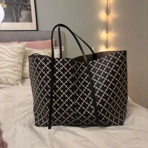 Svart och vit mönstrad shoppingväska - Abi printed tote bag, Använd men fortfarande i okej skick! Se bilder för defekter, slitaget på bandet syns ej när väskan bärs. Går även att justera väskan genom att knyta ihop banden som finns i så blir den något mindre! Pris går att diskuteras Mått: 57 x 33.5 x 16.5 cm ❤️
