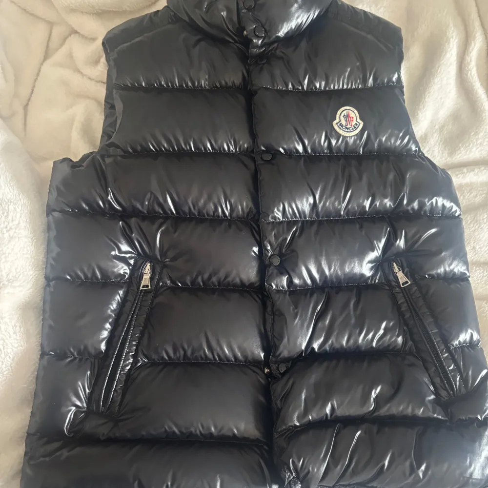 Äkta Moncler Maya Down Vest med glansig finish. Västen har en hög krage och två dragkedjefickor framtill. Perfekt för kyliga dagar när du vill hålla stilen. Moncler-logga på bröstet ger en exklusiv touch.. Takit.