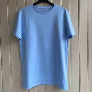 Ralph Lauren T-shirt  - En ljusblå mycket fin Ralph Lauren t-shirt. Mycket fint skick utan fläckar eller skavanker förutom att texten i nacken blev lite sliten av användning. Perfekt inför varma sommardagar☀️  Måtten är ca 70 i längd och 40 i axelbredd.  Om du har några frågor tveka inte på att skriva! 💬