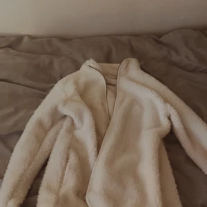 Vit teddyjacka - Mysig vit teddyjacka perfekt för kyliga dagar. Jackan har en fluffig textur och en enkel design utan synliga detaljer som dragkedjor eller knappar. Perfekt för att hålla sig varm och stilren.