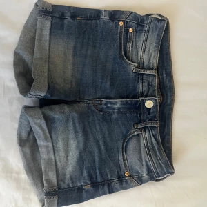 Blå low waist  jeansshorts med uppvikta ben - Blåa low waist jeansshorts i storlek 34. Säljer dem då de är för små för mig.