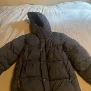 Svart pufferjacka från Dressmann - Säljer en svart pufferjacka från Dressmann i storlek XS. Jackan har en quiltad design med dragkedja och knappar framtill. Perfekt för kalla dagar med sin långa ärmar och skyddande huva. Jätte fin 