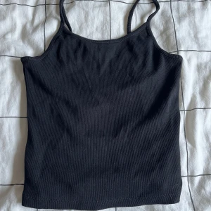 Svart ribbad linnetopp från FB Sister - Snygg svart ribbad linnetopp från FB Sister. Perfekt för en stilren look med smala axelband och en enkel design. Passar bra till både jeans och kjol.