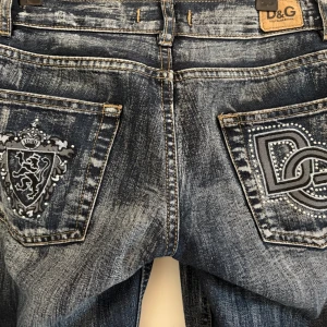 Blå jeans med broderade detaljer från D&G lowwaist bootcut - Snygga blå jeans från dolce and Gabbana med unika broderade detaljer på bakfickorna. Jeansen har en klassisk femficksdesign och en cool tvättad look. Perfekta för dig som vill ha något extra i garderoben! Utsvängda lågmidjade. Mått: midja: 75 cm innerben: 78 cm