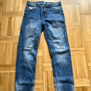 Blå jeans från LAB Industries - Snygga blå jeans från LAB Industries med slitna detaljer på framsidan. De har en klassisk femficksdesign och en knappgylf. Perfekta för en avslappnad stil.