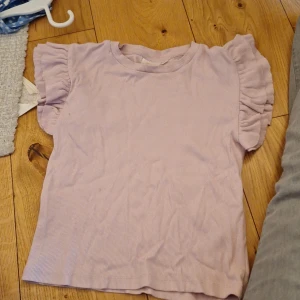 Volangtopp - Säljer en söt ljuslila ribbad topp från Gina Tricot. Toppen har korta ärmar med volangdetaljer som ger en extra touch. Perfekt för en avslappnad stil.