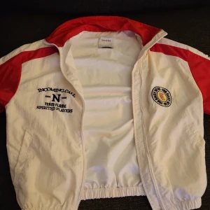 Vit och röd jacka från Bershka - Säljer en cool vit och röd jacka från Bershka med tryck på bröstet och en broderad detalj. Jackan har långa ärmar och dragkedja framtill. Perfekt för en sportig look!