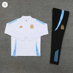 Vit och svart fotbollströja med byxor - Säljer en vit långärmad fotbollströja med blå detaljer och matchande svarta byxor från Adidas. Tröjan har ett tryckt emblem på bröstet och byxorna har blå ränder längs benen. Perfekt för träning eller match! Finns i alla storlekar.