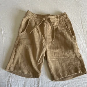 Beige shorts  - Säljer ett par bekväma beige shorts från Kappahl. De har elastisk midja med snörning och praktiska fickor fram och bak. Perfekta för en avslappnad stil. Perfekt för sommaren! 