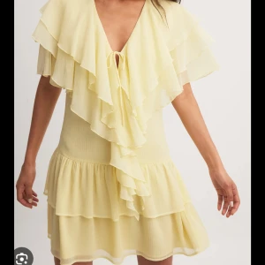 Gul klänning med volanger - Helt ny ljusgul klänning med volanger och v-ringning. Klänningen har korta ärmar och en knytning framtill. Säljer då den var lite för stor på mig.  Prislapp kvar. 