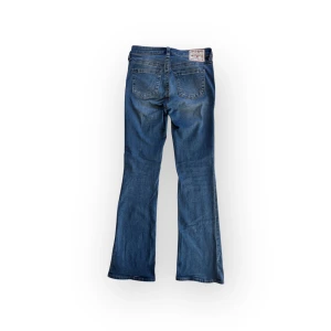 Becca bootcut jeans från True Religion - Snygga blå bootcut jeans från True Religion med klassisk femficksdesign och knappgylf. Inga tydliga defekter. Storlek W28 passar S-M. Midja 38 innerben 80