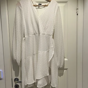 Vit omlottklänning från Vero Moda - Säljer en elegant vit omlottklänning från Vero Moda. Klänningen har långa ärmar och ett knytband i midjan. Den är dekorerad med ett prickigt mönster och har en v-ringad hals. Perfekt för sommarens tillfällen! Bara använd 1 gång!