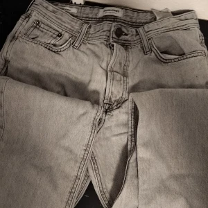 Grå jeans från Jack & Jones - Säljer ett par grå jeans från Jack & Jones med en loose passform. De har en klassisk femficksdesign och är tillverkade i denim. Perfekta för en avslappnad stil.
