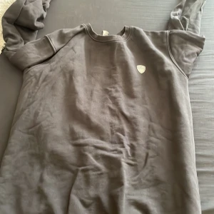 Svart tröja från Emporio Armani - Snygg svart tröja från Emporio Armani med ett stort tryck på baksidan. Tröjan har långa ärmar och en rund halsringning. Perfekt för en stilren look.