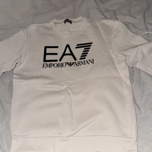 Vit sweatshirt från Emporio Armani - Säljer en stilren beige sweatshirt från Emporio Armani med det ikoniska EA7-logotypen tryckt på framsidan. Tröjan har en rund halsringning och långa ärmar, perfekt för en avslappnad look. Passar bra till både jeans och joggers. Vid intresse bara att skriva 