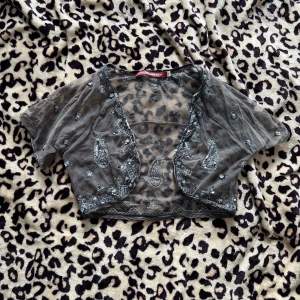 Svart bolerotopp från Indiska - Säljer en elegant svart bolerotopp från Indiska. Den är dekorerad med glittriga paljetter och har ett vackert broderat mönster. Perfekt för att lägga till lite glamour till din outfit.