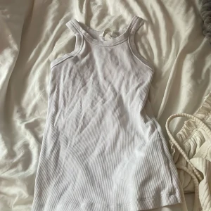 Vit ribbad linnetopp - Säljer en stilren vit ribbad linnetopp med breda axelband. Perfekt för varma sommardagar eller som ett basplagg i garderoben. Toppen har en enkel och klassisk design som passar till det mesta.