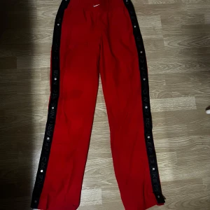 Röda träningsbyxor från Nike - Snygga röda träningsbyxor från Nike med svarta sidopaneler och texten 'NIKE PRO'. Byxorna har en elastisk midja och är perfekta för träning. De har en avslappnad passform och är gjorda i ett lätt material.
