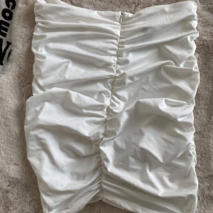 Vit kortkjol med rynkdetaljer - Säljer en stilren vit kortkjol med snygga rynkdetaljer. Kjolen har en tight passform och är perfekt för att skapa en chic look. Materialet är mjukt och bekvämt, vilket gör den idealisk för varmare dagar.